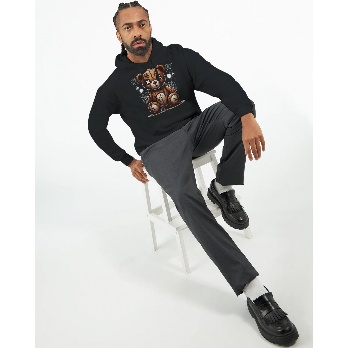 Man sitting on a stool wearing a black men's teddy bear hoodie, gray pants, and black shoes. 7