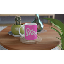 Pink Stay True mug with white cursive slogan on a wooden table beside a small cactus.