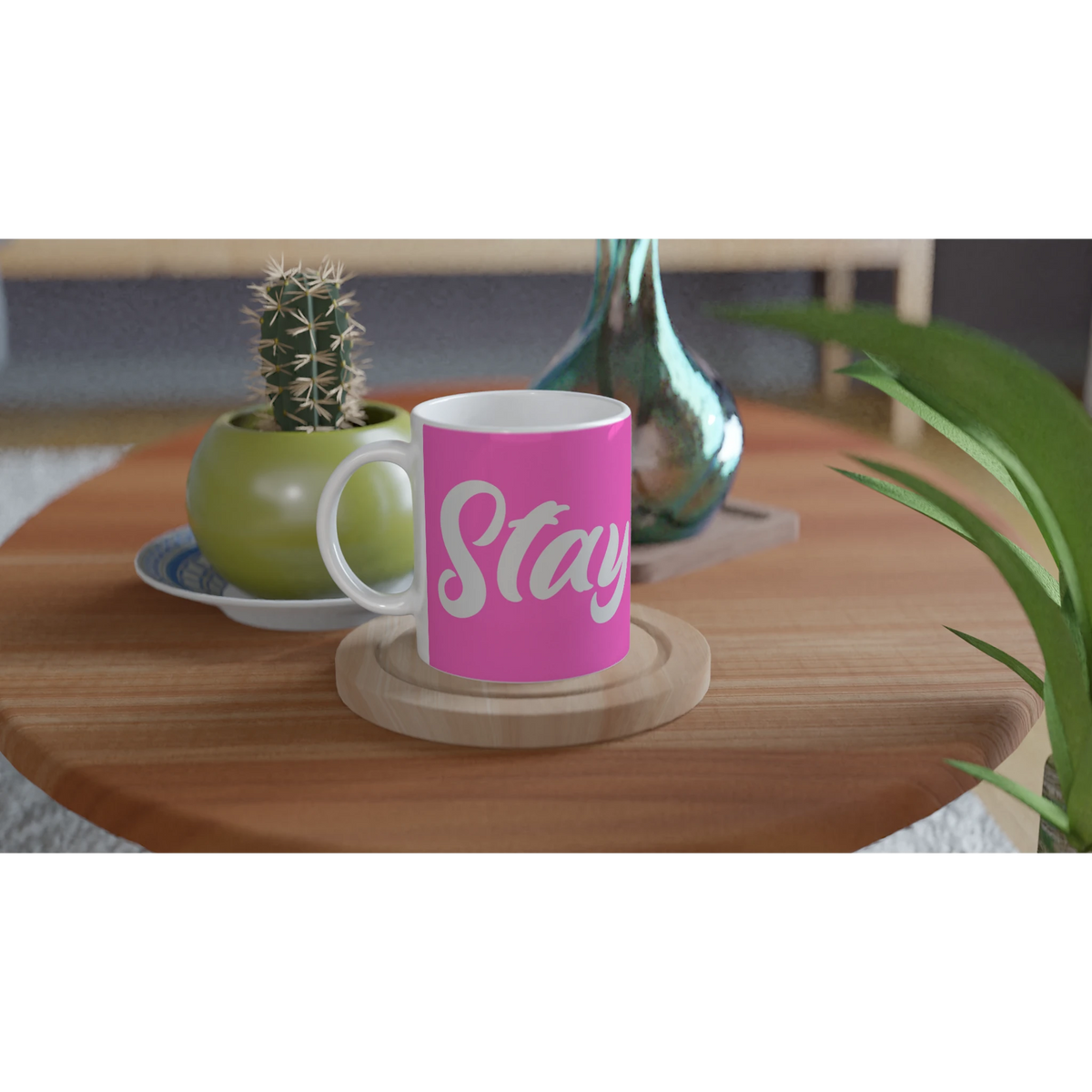 Pink Stay True mug with white cursive slogan on a wooden table beside a small cactus.