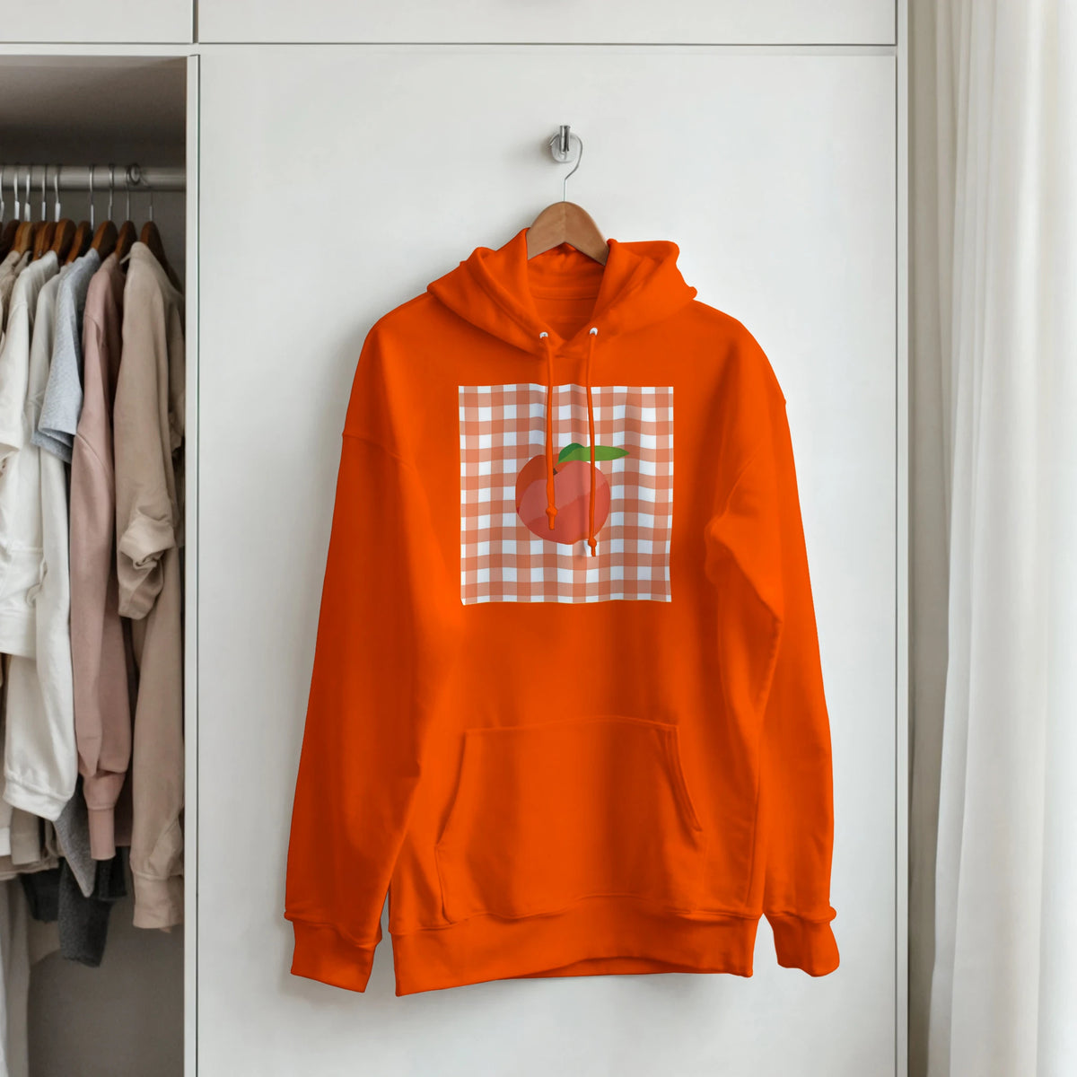 Orange hoodie featuring a retro peach graphic set against a peach and white gingham square, hanging on a wooden hanger.