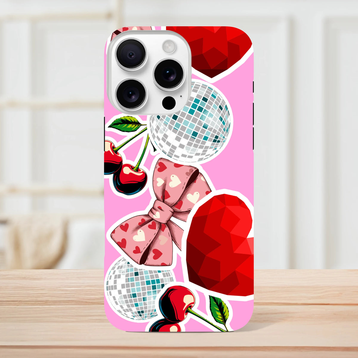 Pink iPhone case featuring sticker-style cherries, heart-patterned bow, disco balls, and faceted red hearts in a bold Y2K design.