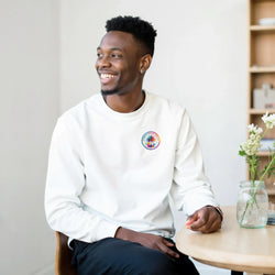 Man wearing white crewneck sweatshirt featuring colorful circular Urban Palm Trees graphic logo on the chest.