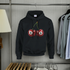 Black hoodie with cherry design featuring number 8 on hangers against a gray wall.