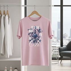 Pink t-shirt with floral design and text hanging on a wooden hanger in a room with white walls and a cityscape view.
