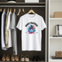 White t-shirt with colorful palm tree design hanging in a wardrobe with clothes and shoes.