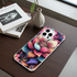 Colorful floral phone case on a wooden surface with books and a vase.