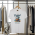 White t-shirt with coconut graphic design hanging on a rack with other clothes.