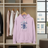 Pink hoodie with floral design and text on a wooden rack with other clothes.